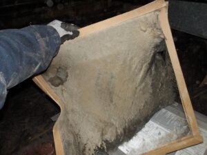 Inspector holding a heavily clogged, dust-covered furnace filter